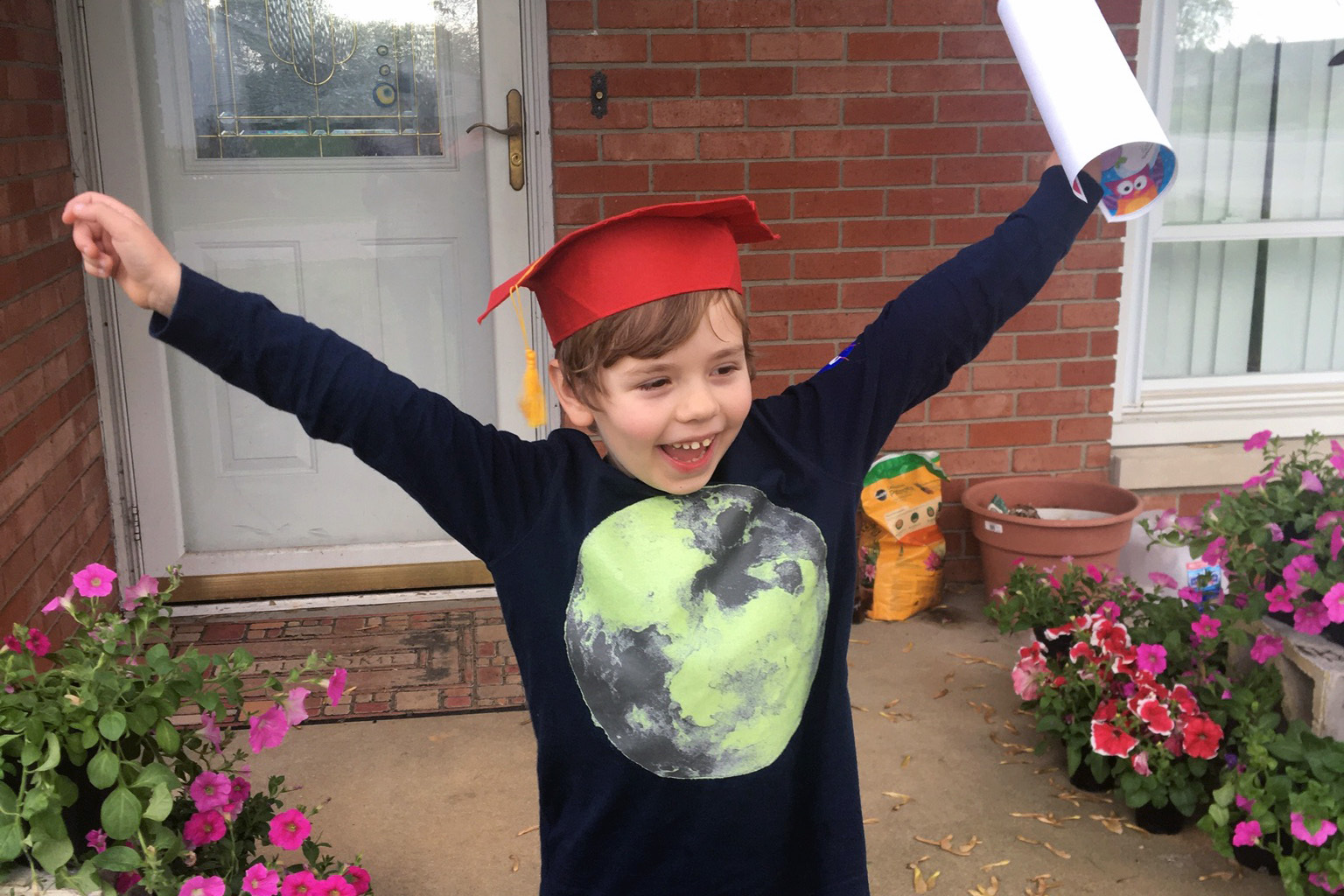 A young boy wears a red graduation cap with his arms outstretched, and a look of absolute glee across his face. Suzanne Godby Ingalsbe's son Nicholas graduated from kindergarten in the spring 2020 and started first grade remotely this year. He likes playing games with his friends online, but misses things like summer camp and spending time with friends on the bus. Provided by Suzanne Godby Ingalsbe.