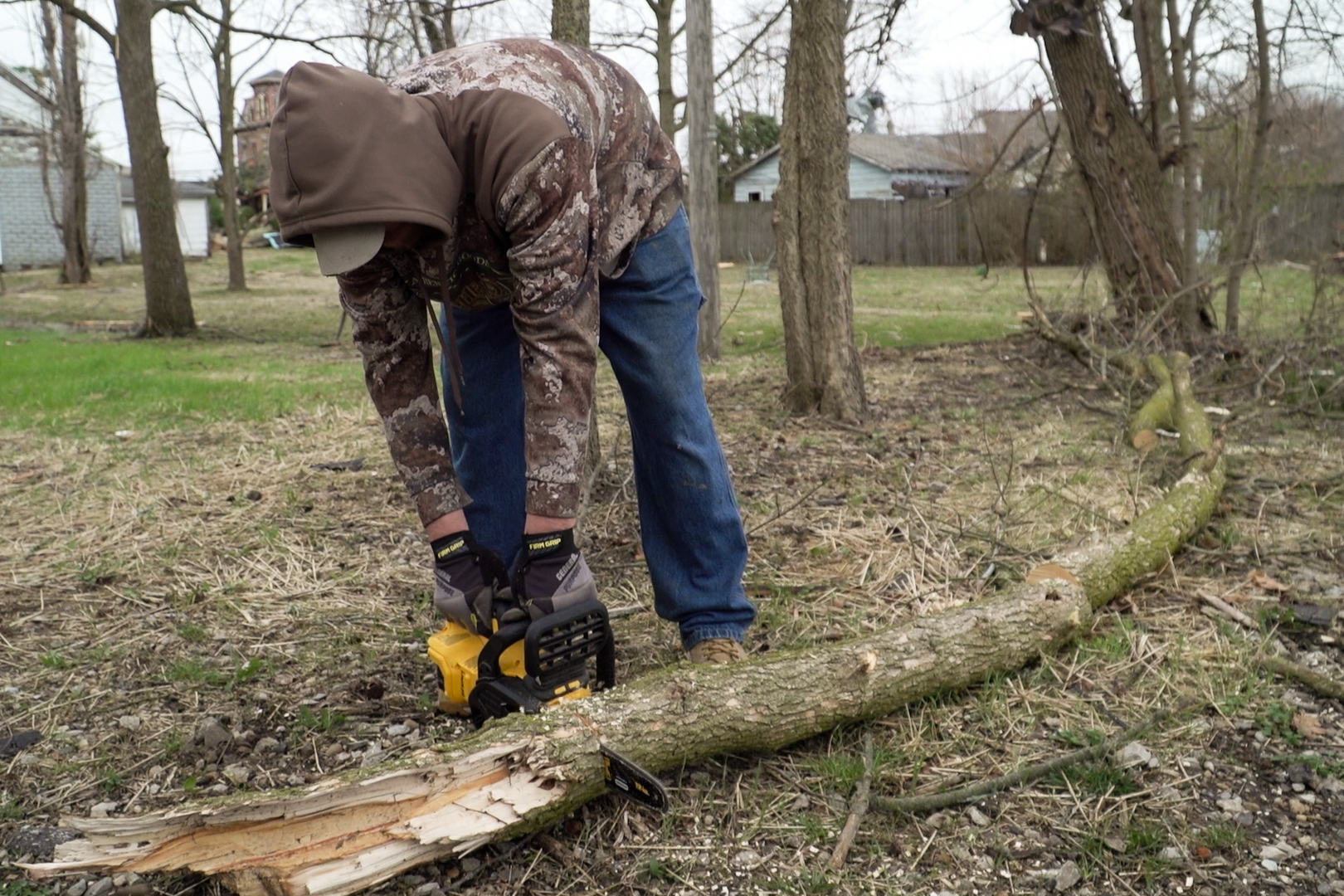 A man uses a chainsaw to break down branches to move away from damaged property.